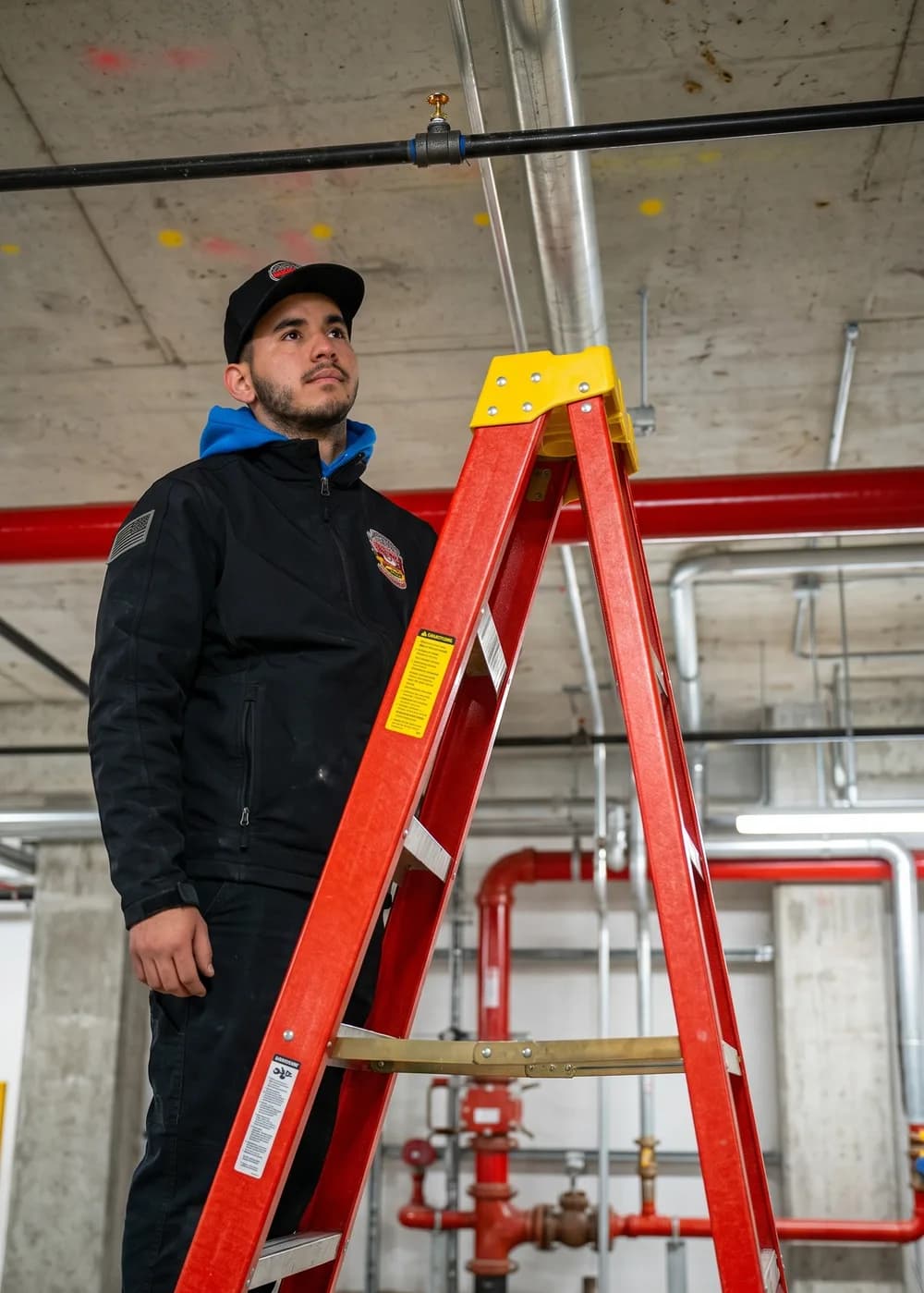 County Fire technician inspecting a fire sprinkler head from a ladder