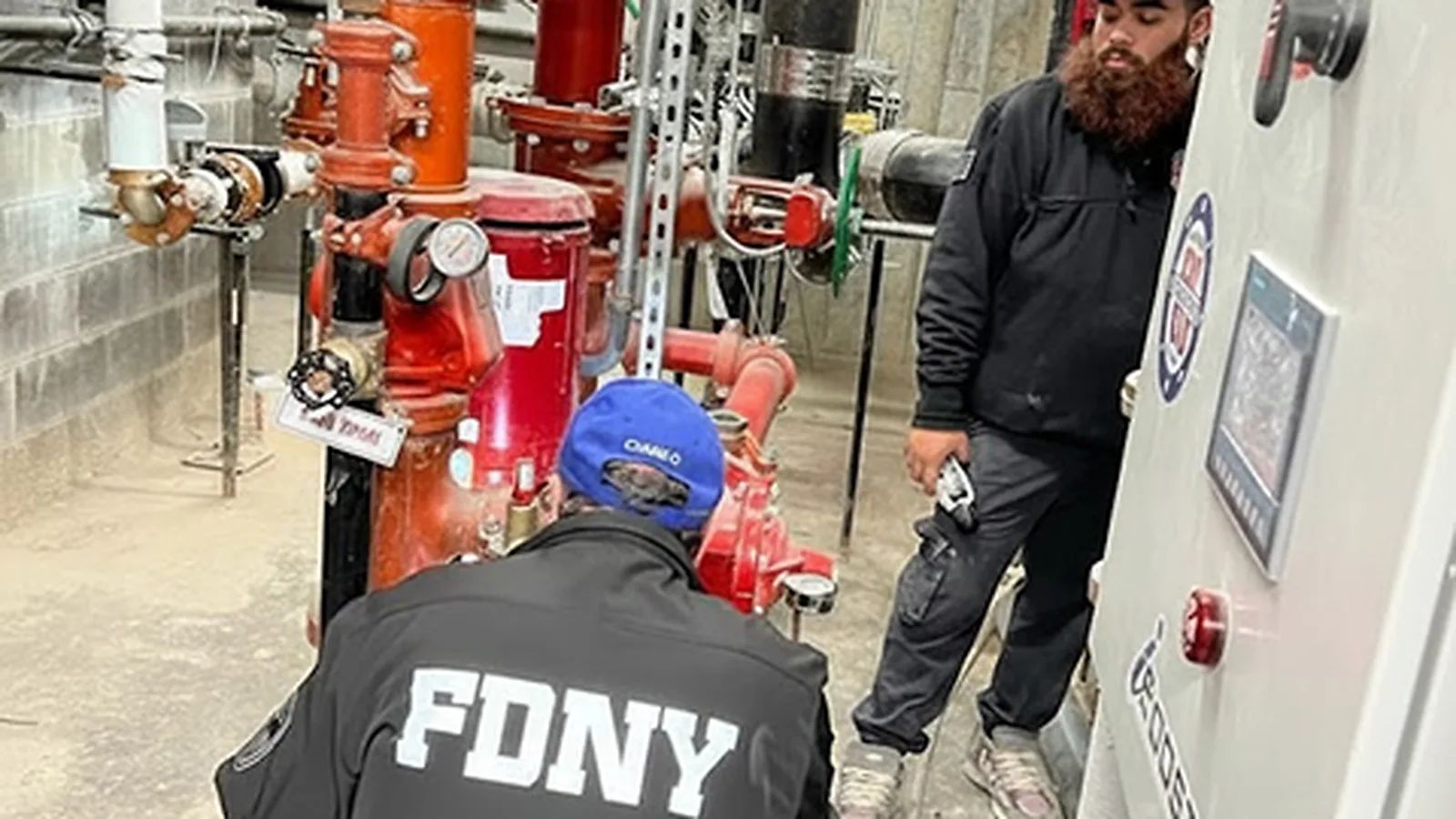 An FDNY inspector examining a fire pump assembly alongside a County Fire technician during a commercial property inspection