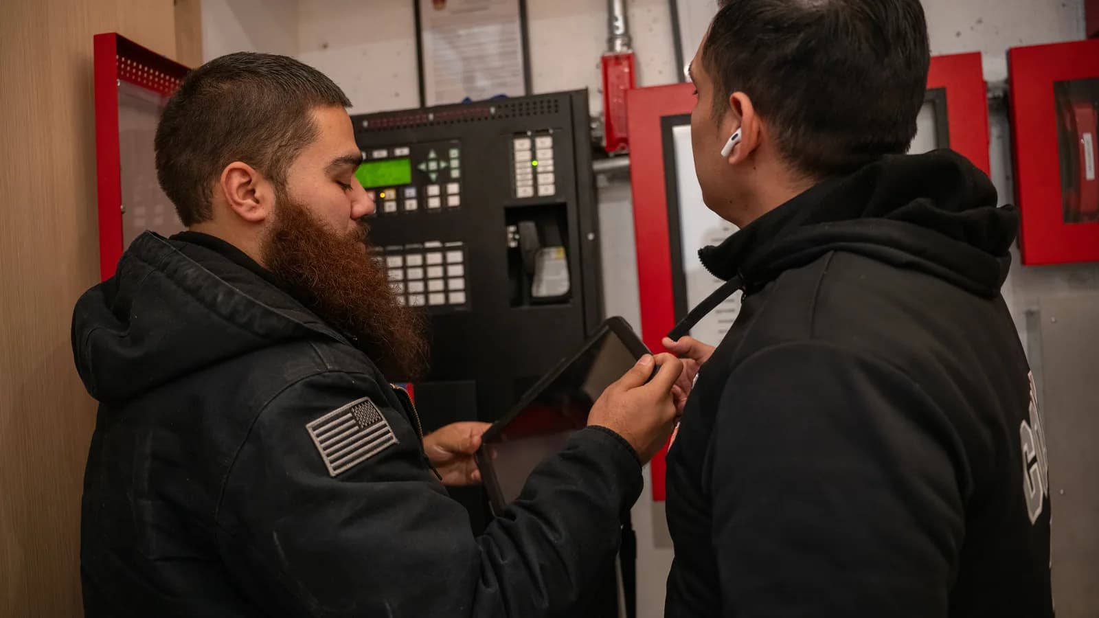 Two County Fire technicians reviewing a fire alarm control panel on a tablet during a violation clearance visit