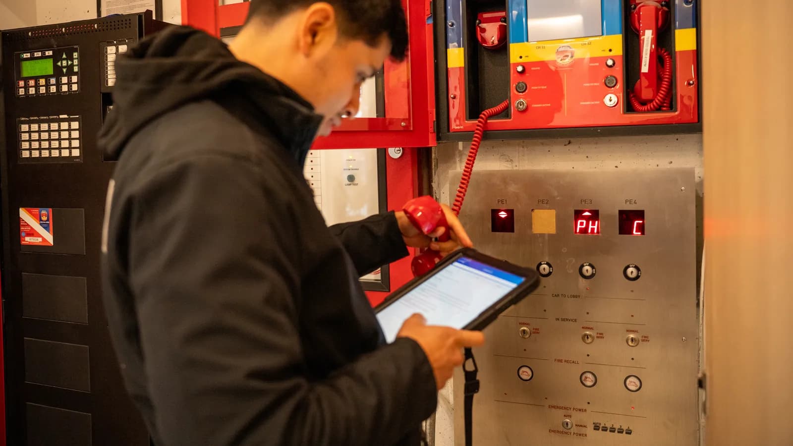 A County Fire technician logging results on a tablet while testing a fire alarm and auxiliary radio communication panel