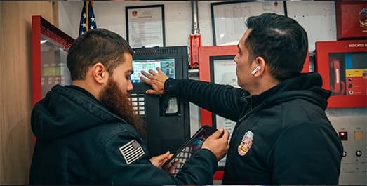 County Fire technicians reviewing a fire alarm and BDA panel in an NYC building