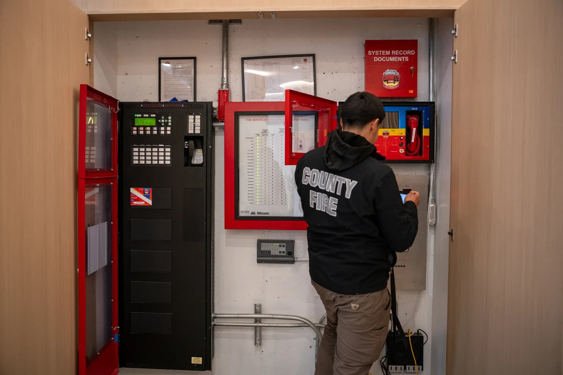 A County Fire technician inspecting a fire alarm control panel and ARCS in a Brooklyn commercial building