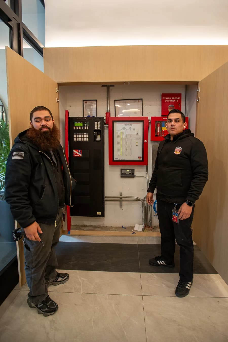 Two County Fire technicians next to a completed fire alarm and BDA panel installation