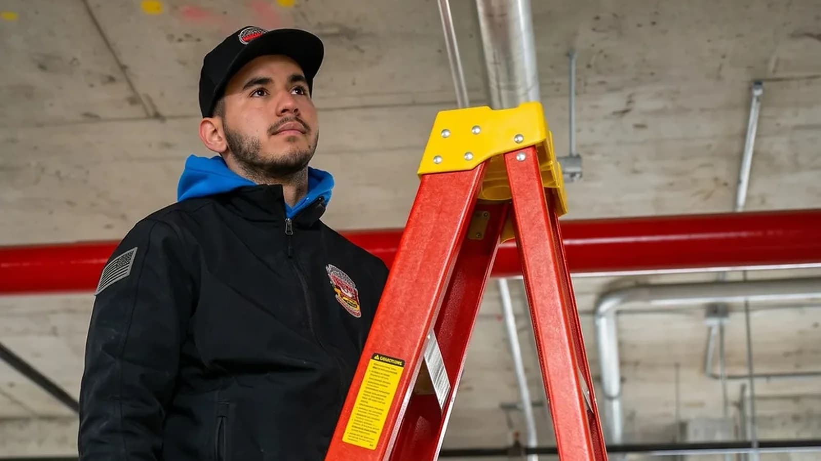 County Fire technician on a ladder inspecting overhead sprinkler piping and heads