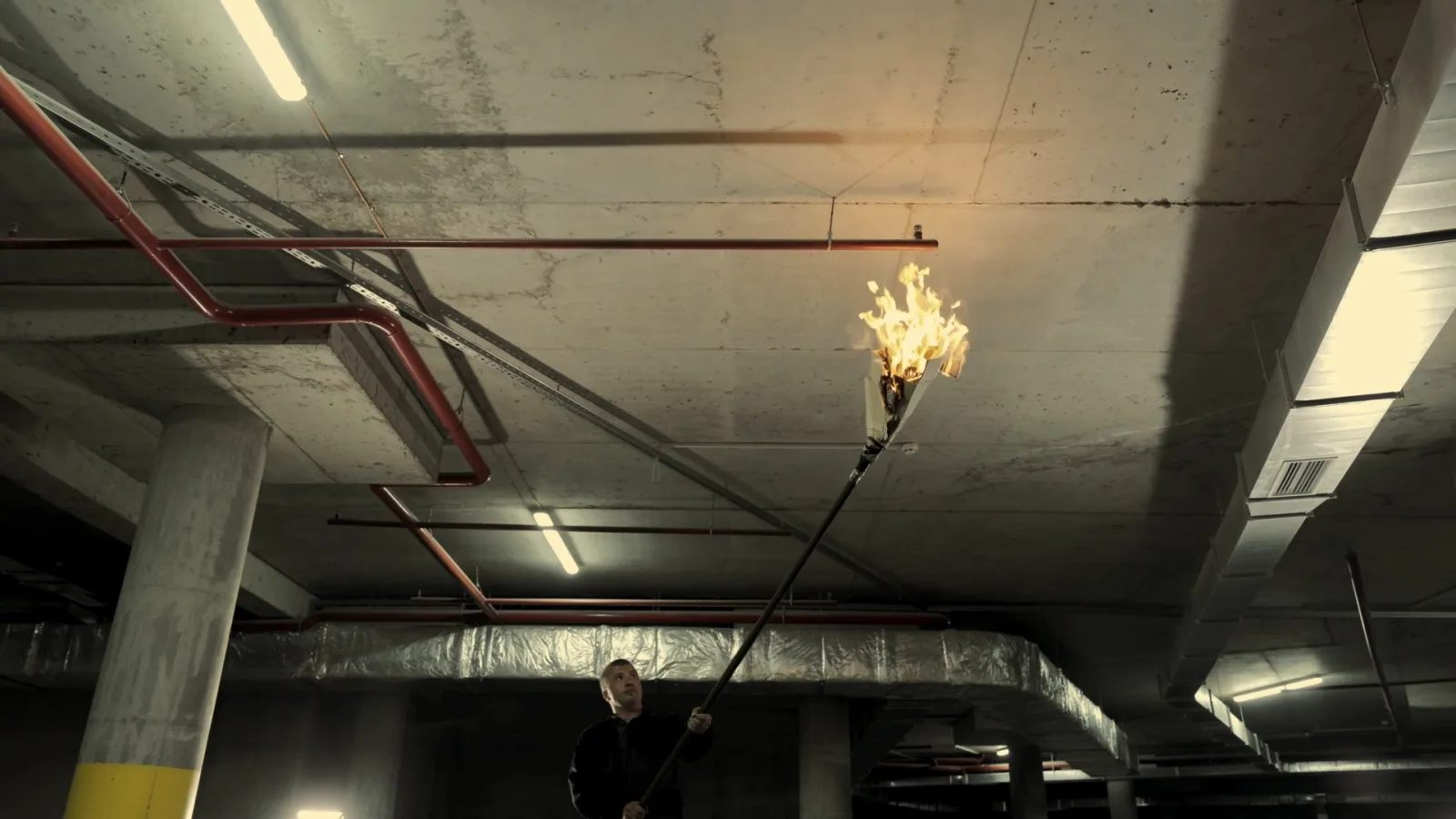 A pole-mounted flame held to a parking garage ceiling beside a pendent sprinkler head
